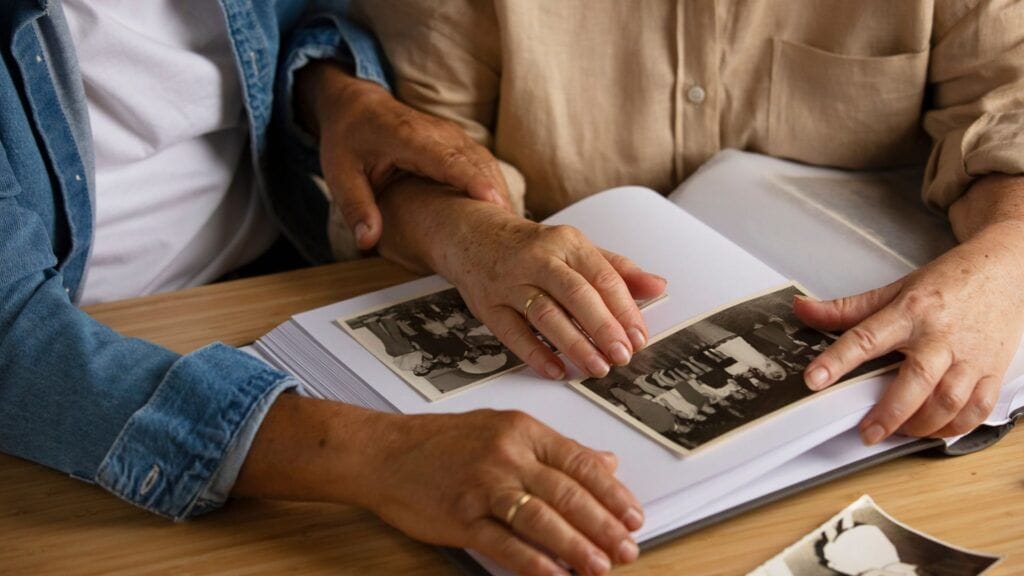 Compra de derechos hereditarios en herencias argentinas con herederos en España Dos personas mayores revisan un álbum con fotografías antiguas sobre una mesa, en una escena vinculada al recuerdo familiar y la herencia.